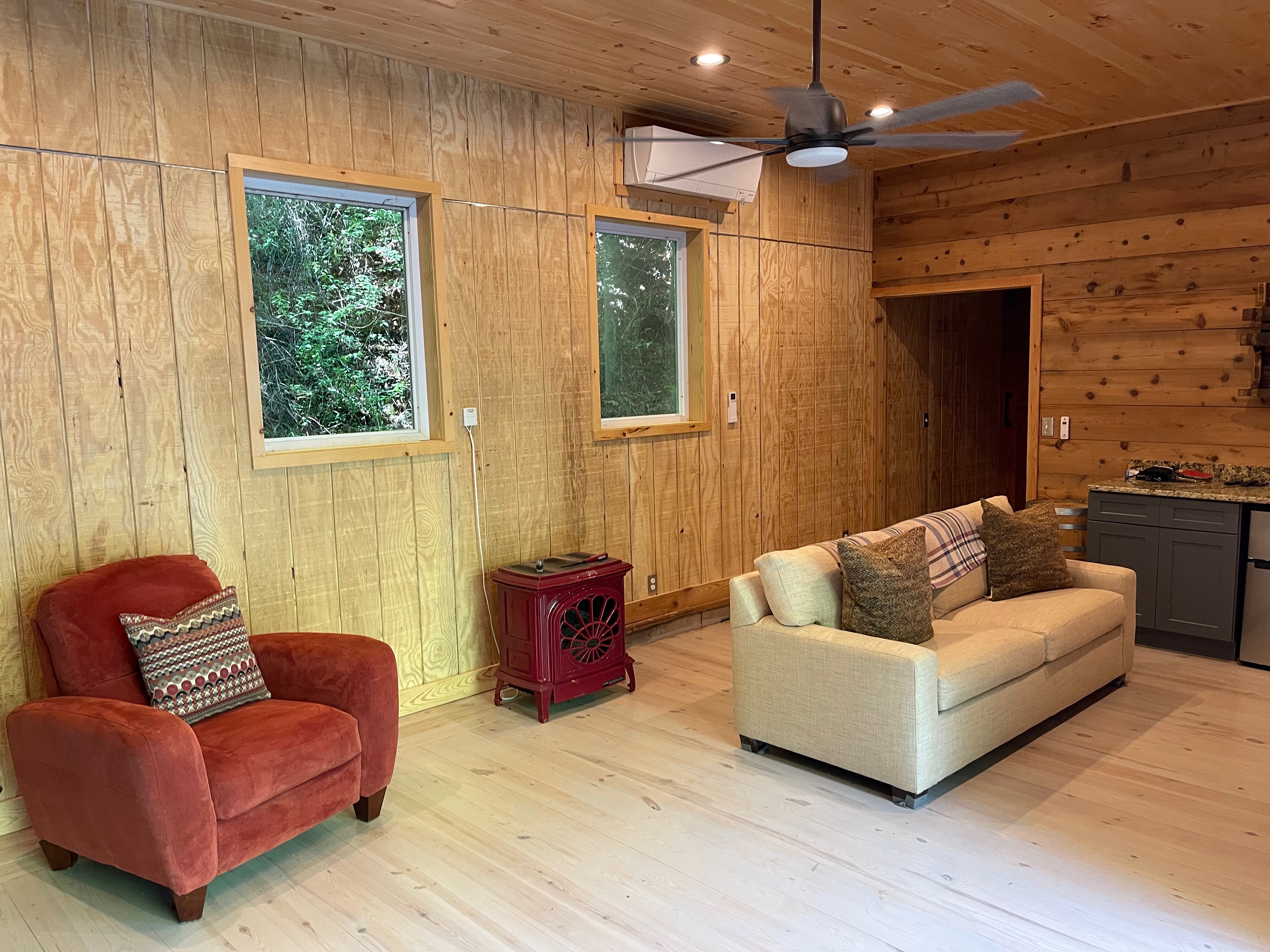 Wood-paneled game room with red armchair, sofa, and forest views